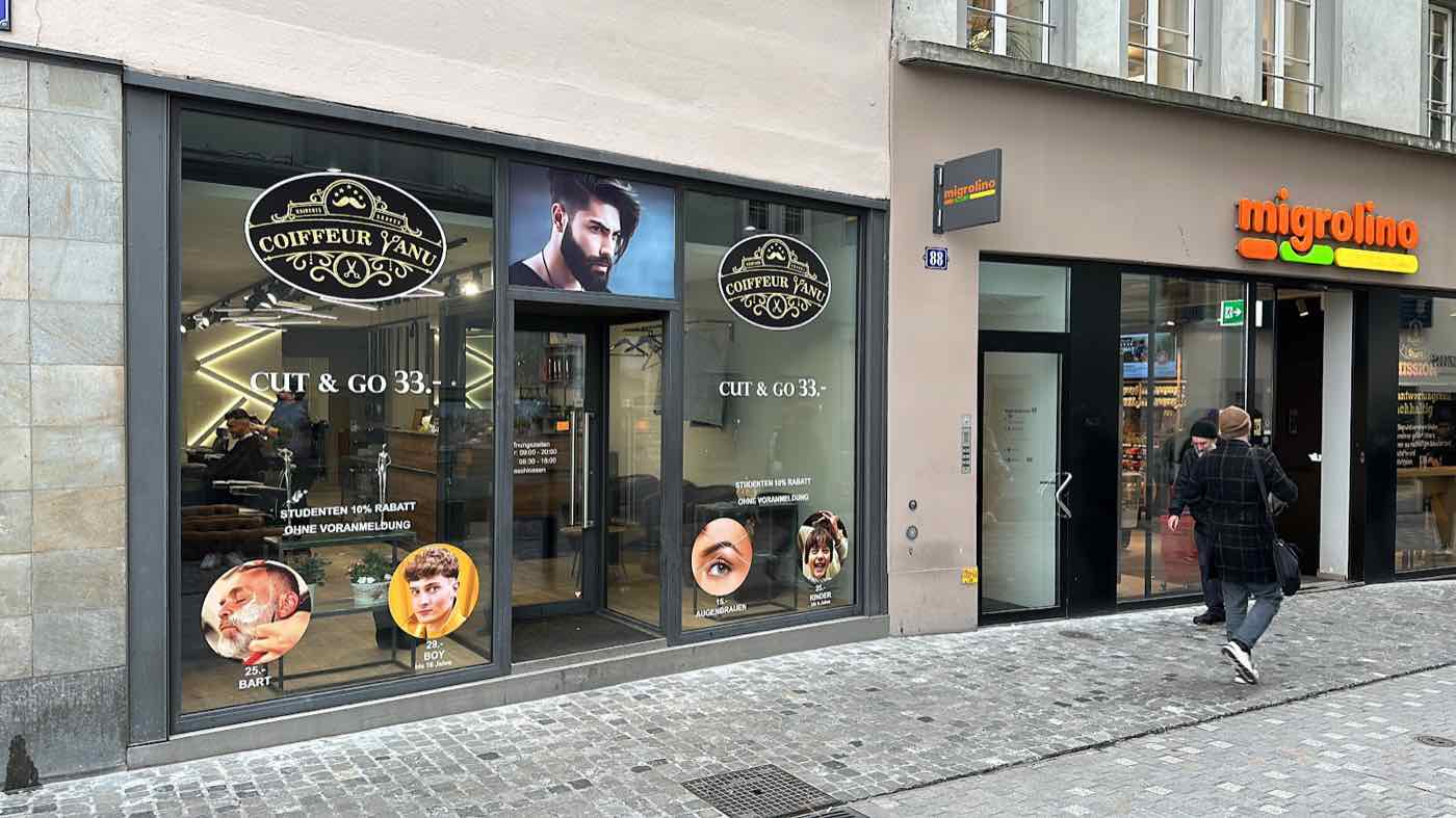 Ladenfront von Coiffeur Yanu Central an der Niederdorfstrasse in Zürich, mit dem schwarz-goldenen Badge-Logo im Schaufenster